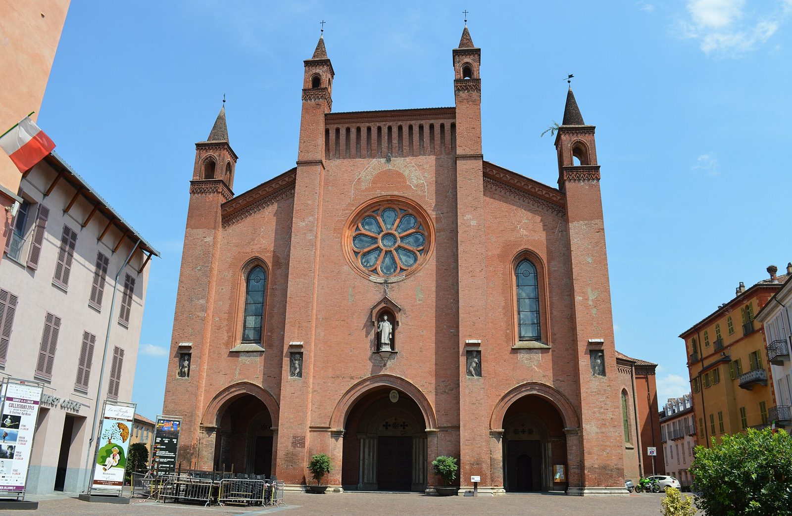 La facciata in mattoni del Duomo di San Lorenzo ad Alba, con il rosone centrale, i tre portali e i quattro pinnacoli, sotto un cielo azzurro