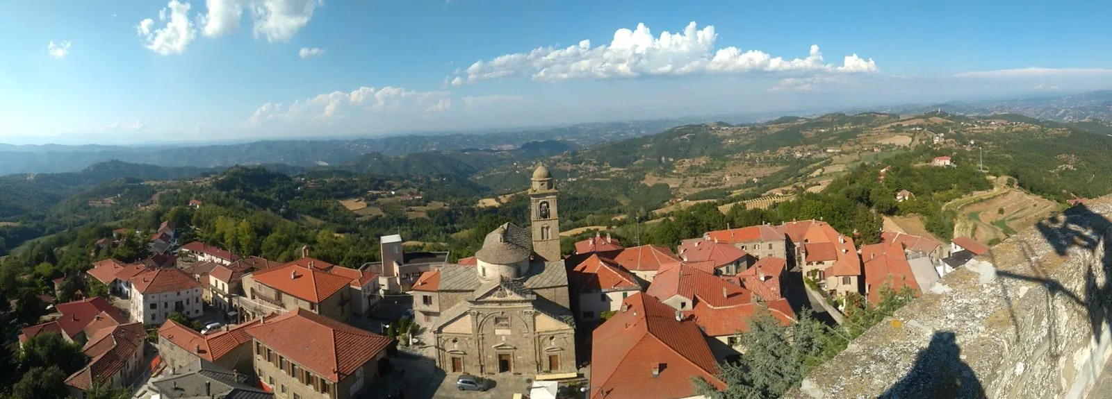 Veduta dall'alto di Roccaverano, con i tetti rossi del borgo, la chiesa parrocchiale con la cupola e le colline della Langa Astigiana fino all'orizzonte